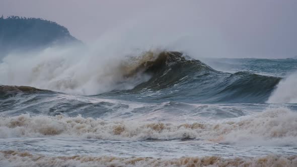 Big Wave with Foam and Dirt Moves in the Sea and Breaks on the Rock During Strong Storm