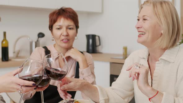 Three Mature Women Toasting with Glasses of Red Wine at Kitchen Table