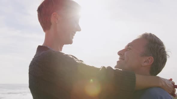 Caucasian couple enjoying free time by sea on sunny day embracing and smiling