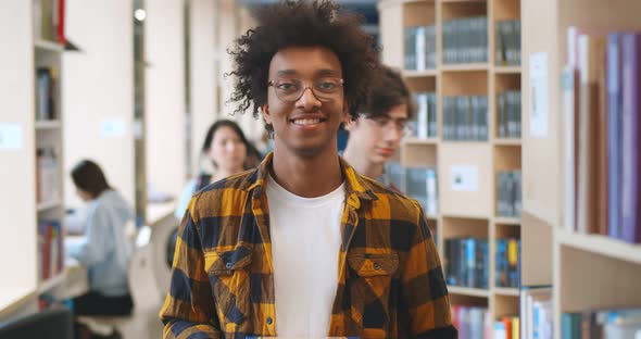 Confident Handsome African Student Smiling at Camera with Library Bookshelves on Background
