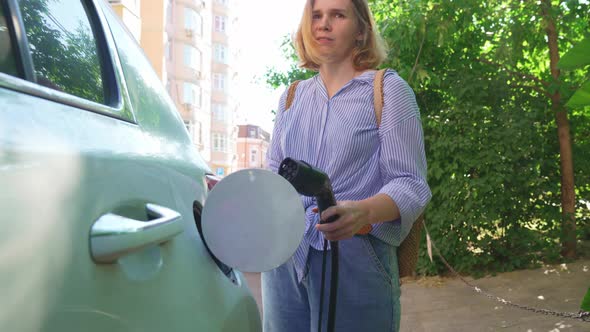 Woman Plugging in an Electric Car at Outlet Socket