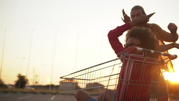 Multiethnic Couple Bearded Guy Circling Funny Afro American Girl with Curly Hair in Shopping Trolley