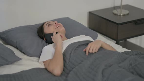 Hispanic Woman Talking on Phone while Sleeping in Bed