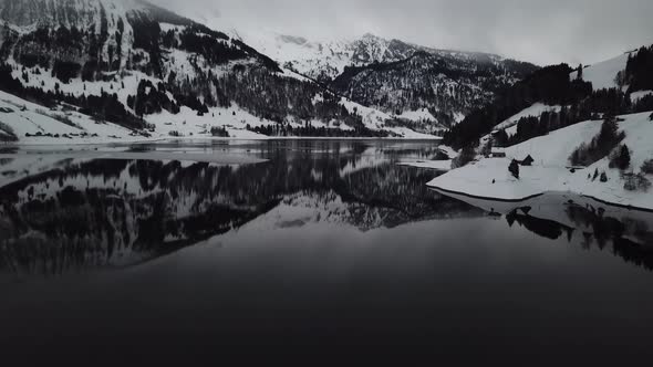 Camera flying backwards and tilting up to show the beautiful winter mountain lake panorama in Switze