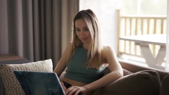 Blonde Woman Sitting on Sofa in Country House Browsing Social Media on Laptop