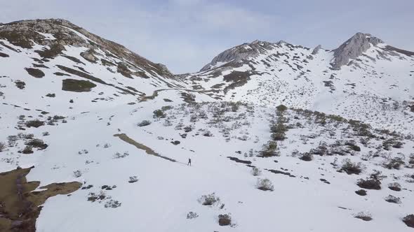Aerial view of man hiking to top of snow-capped mountains in winter