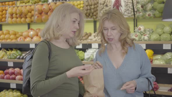 Portrait of Two Confident Caucasian Housewives Discussing Purchases in Grocery Store. Senior Blond
