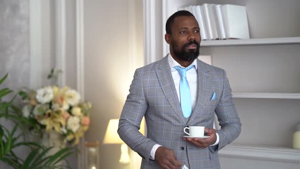 a Bearded AfricanAmerican Man in a Plaid Suit with a Blue Tie Stands Thoughtfully with a Coffee Cup