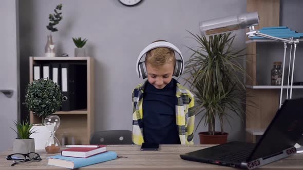 Cheerful Funny Teen Boy in Headphones which Enjoying Music and Dancing Near the Table