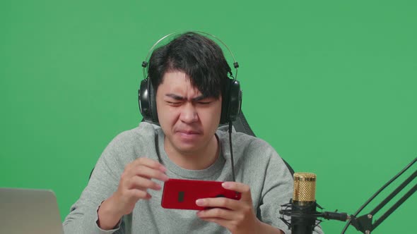 Upset Asian Man Gamer With Headphone Losing Mobile Phone Game On The Green Screen Background