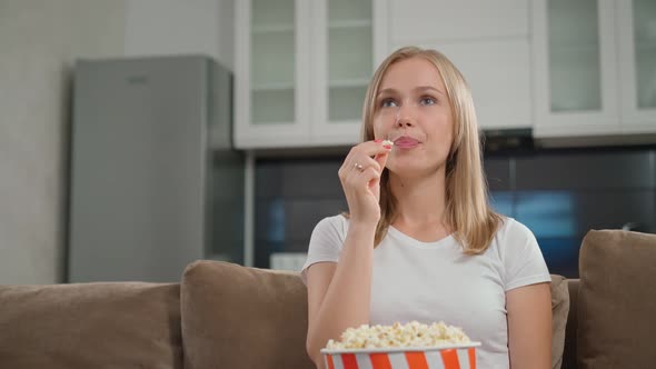 Young Blonde Watching Film and Eating Popcorn on Couch