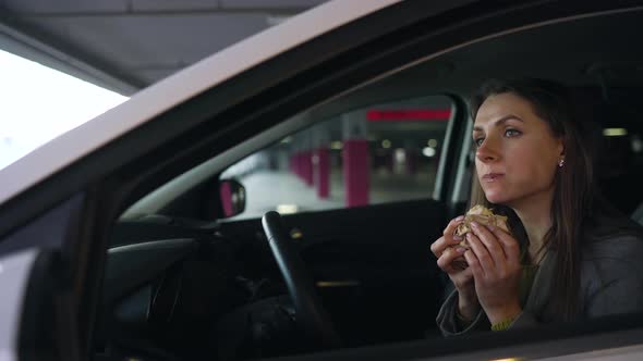 Woman Eating Sandwich Sitting in the Car on the Parking