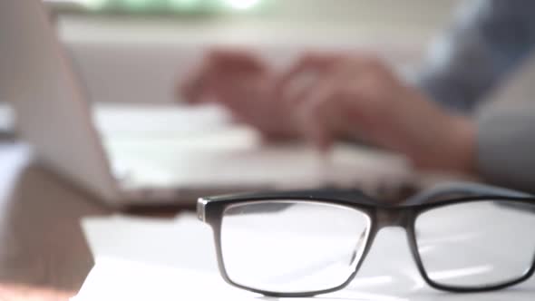 The Eyeglasses Lie on the Table in Front of the Laptop