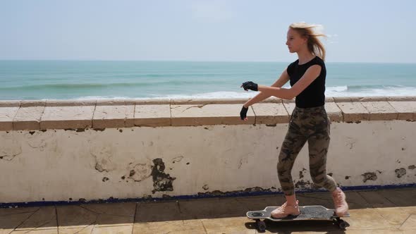 A Beautiful Blonde Girl on Skateboard in Summer Hot Day on Seafront