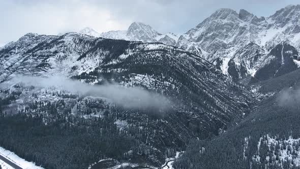 Drone capturing high mountains in snow, black forest small cloud in Kananaskis, Alberta, Canada