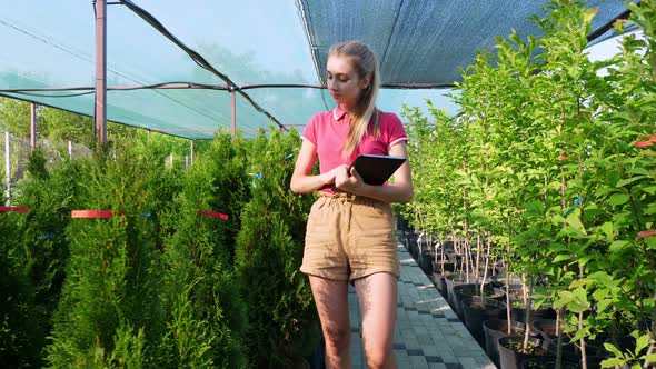 Female Gardener Checks Quality of Plants, Takes Notes on Digital Tablet, Walking Along Garden Center