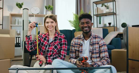 Couple which Sitting on the Floor in New Bought Apartment and Posing on Camera with Tape Measure