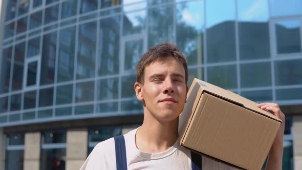 The Courier Carries a Box on His Shoulder Against the Background of a Glass Modern Highrise Building