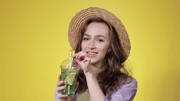 Surprised Woman Drink Mojito cocktail From Plastic Cup Over Yellow Studio Background