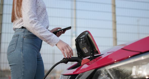 Woman Plugs in Charger into Socket of Her Modern New Red Electric Car