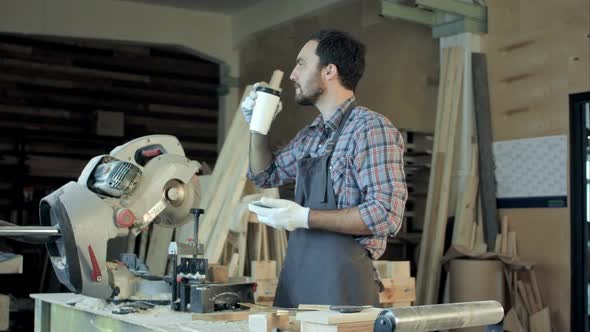 Carpenter Standing Near Electric Saw in His Workshop and Drinking Coffee