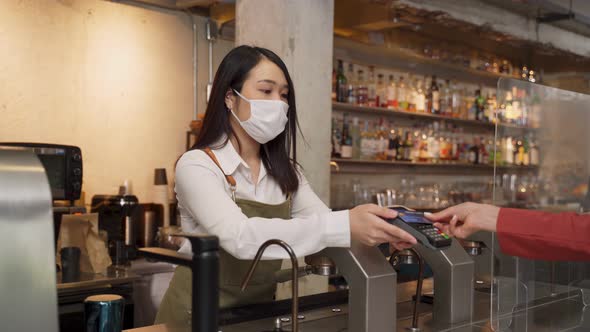 Woman customer paying touchless credit card to waitress with face mask on counter in restaurant.