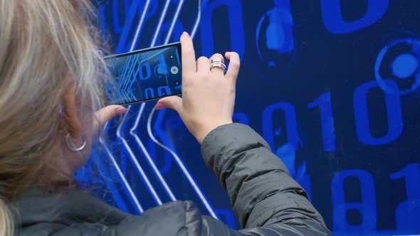 A Woman Shoots a Video on a Smartphone Symbols in the Form of a Binary Code on a Blue Background