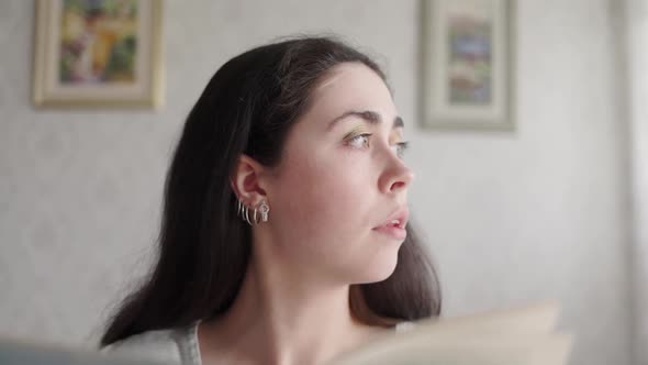 A young woman reads a book, and looks away.