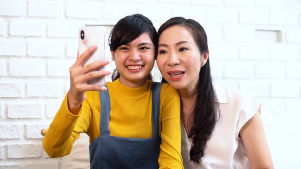 Happy Asian Teenage Daughter and Middleaged Mother Taking Video Calling