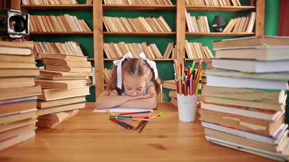 Portrait of a Tired Young Blond Girl Teaches Lessons with a Notebook at Table in the School