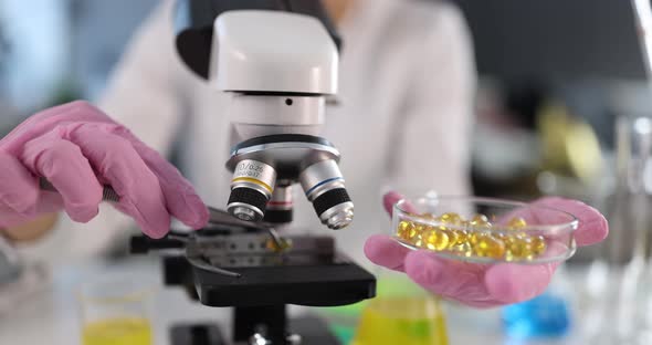 Scientist Examines Yellow Oily Capsules on Microscope Closeup