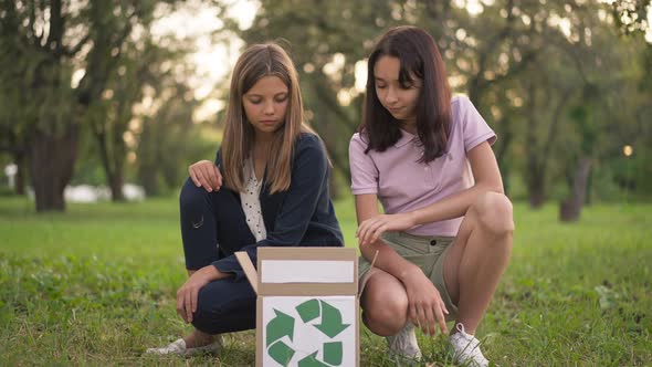 Wide Shot Proud Teen Ecoactivists Sitting at Box with Recycle Sign Looking Inside