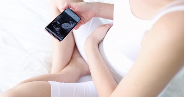 Pregnant Woman Looks at Ultrasound of Fetus on Smartphone