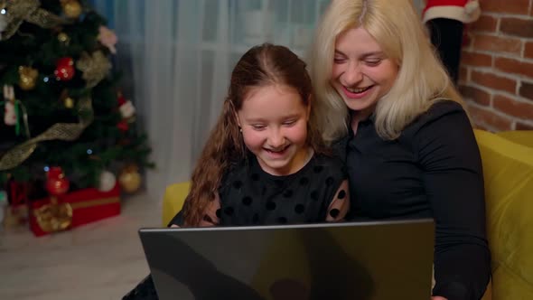 Females persons sitting on sofa and using laptop at home indoors. Mother and daughter having fun