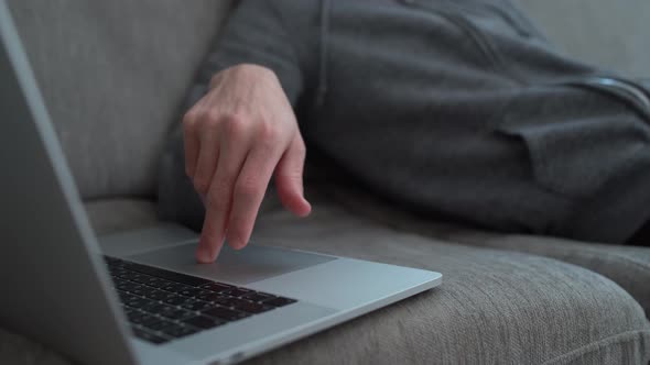 Tired guy typing slowly on his computer while sitting on couch