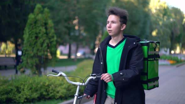 Delivery Man with Green Backpack Rides a Bicycle Through the City with Food Delivery