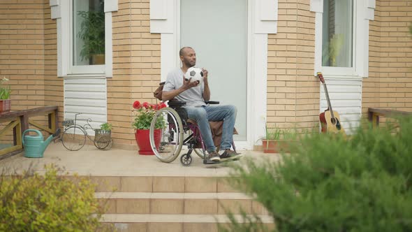 Extreme Wide Shot of Hopeful Handicapped African American Man in Wheelchair Spinning Soccer Ball on