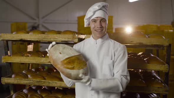 Baker in Uniform Showing Large Round Loaf of Bread with Image of Smile at Camera