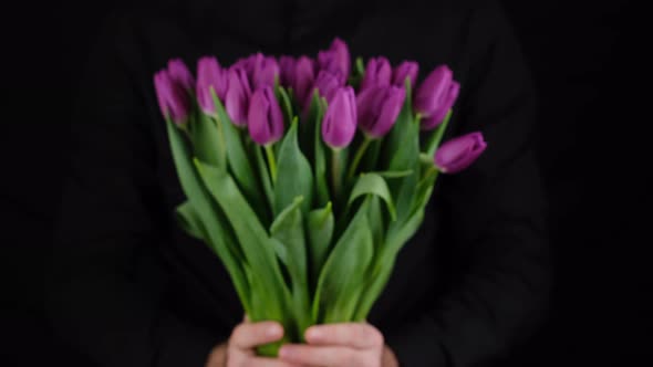 man in black shirt give bouquet of flowers purple tulips