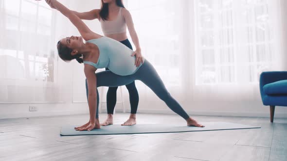 Pregnant woman doing yoga exercise with personal trainer at home.