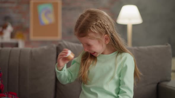 Joyful Little Girl Shakes Bottle with Golden Glitter on Sofa