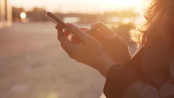 Young attractive business woman sitting outdoor on the bench and using smartphone.