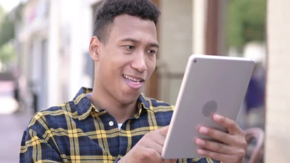 Young African Man Cheering Success on Tablet Outdoor