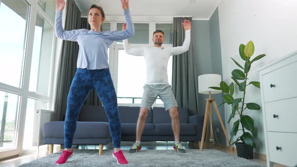 Caucasian Couple is Doing Jumping Jacks Exercise at Home in Cozy Bright Room Slow Motion