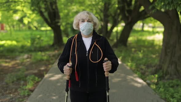 Active Senior Old Woman in Mask Training Nordic Walking in Park at Quarantine