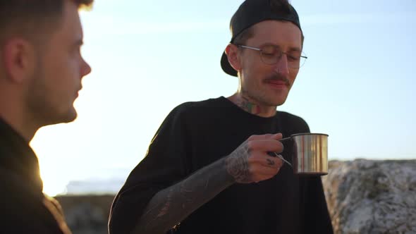 Two Young Guys in Black Clothes Talking and Tasting Coffee on Seashore Slow Motion