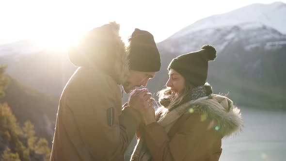 Young Couple in Winter Coats Standingto Each Other Holding Hands Towards Gorgeous Snowy Mountains