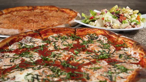 Large cheese pizza large Margherita pizza and Italian chef salad on tabletop, slider 4K