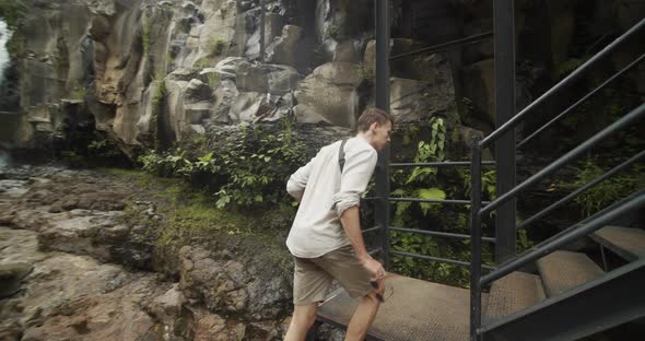 Low Angle Shot Following a Young Male in Tropical Jungle Walking Away From the Waterfall and Up a