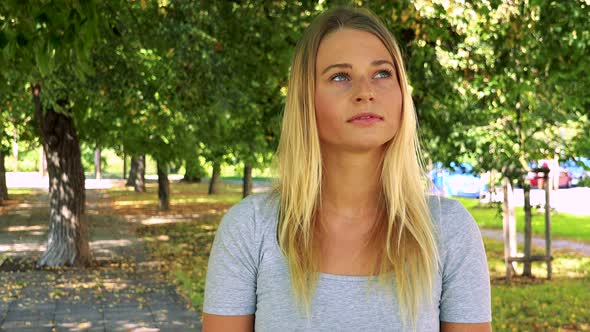 Young Pretty Blond Woman Looks Around - Park with Trees in Background